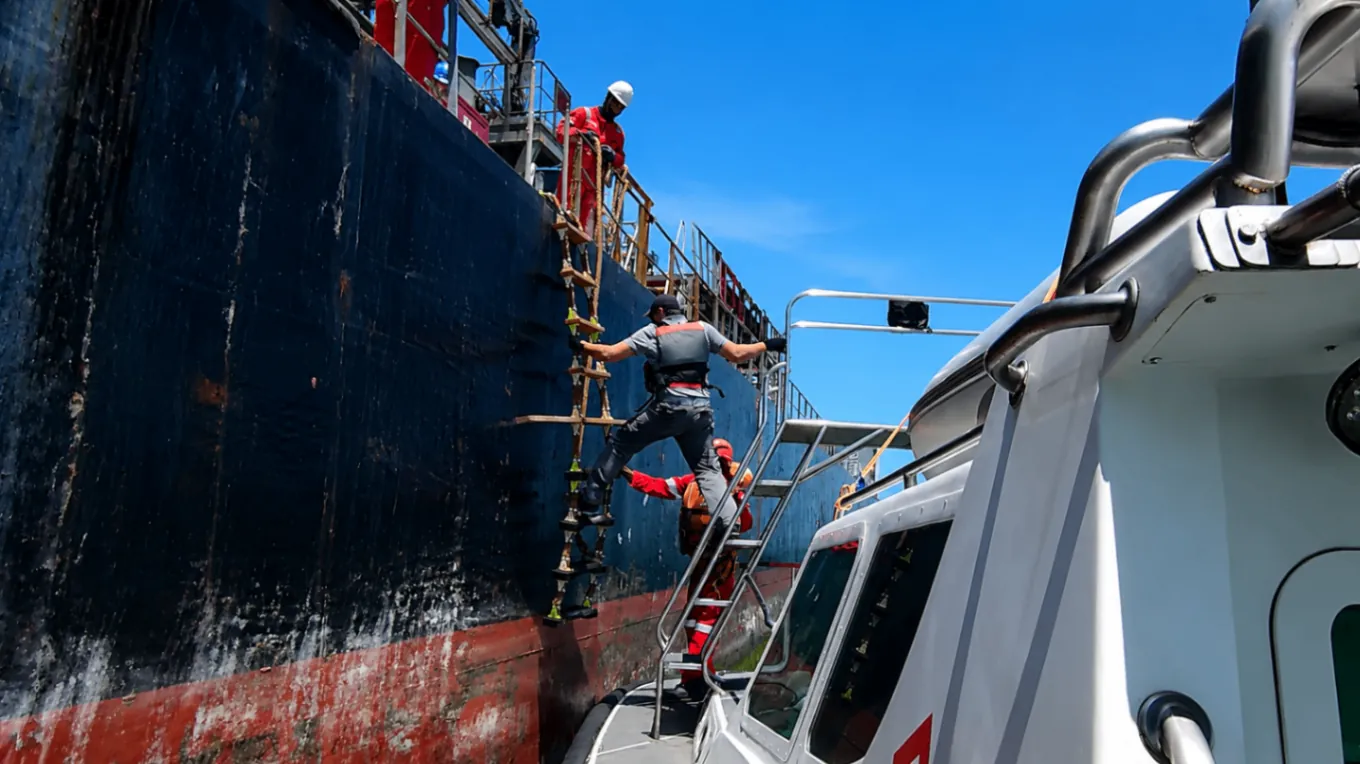Prático marítimo subindo escada de prático no costado de navio cargueiro