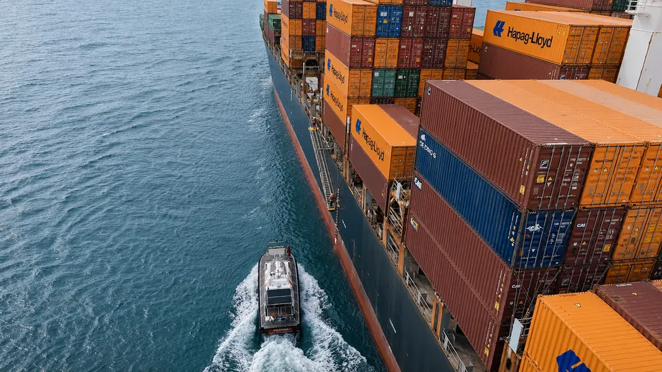Lancha de prático seguindo navio porta-contêineres em manobra